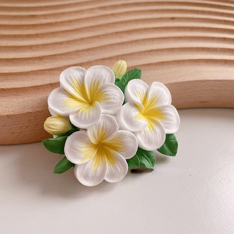 Flower-shaped hair clip with white and yellow flowers on a wooden background